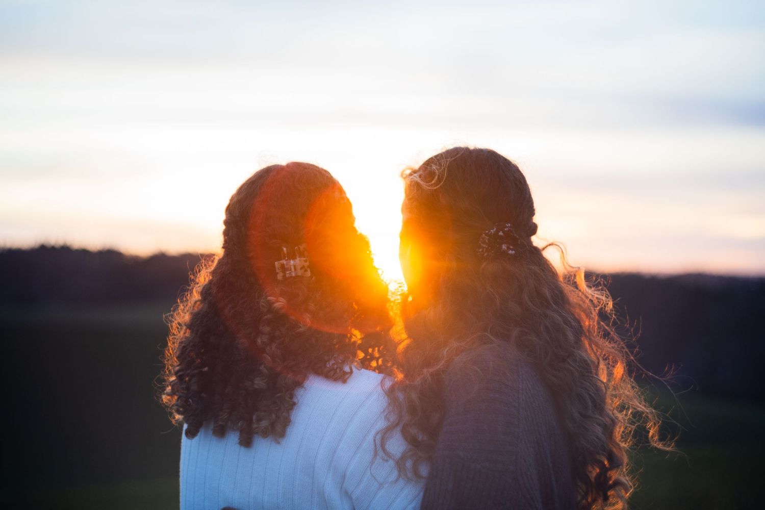 Two silhouettes stand together against a vibrant sunset backlit by golden light.