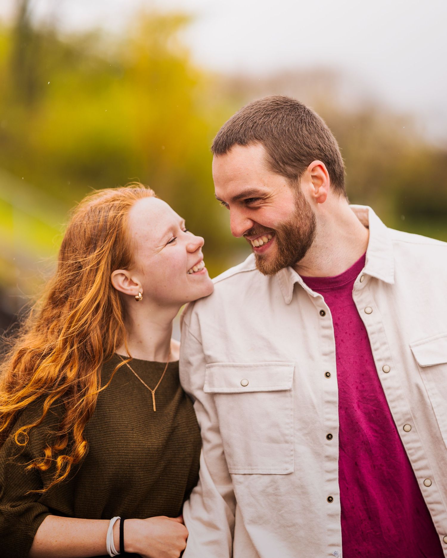 A couple laughing together during an autumn photoshoot with golden foliage in the background.