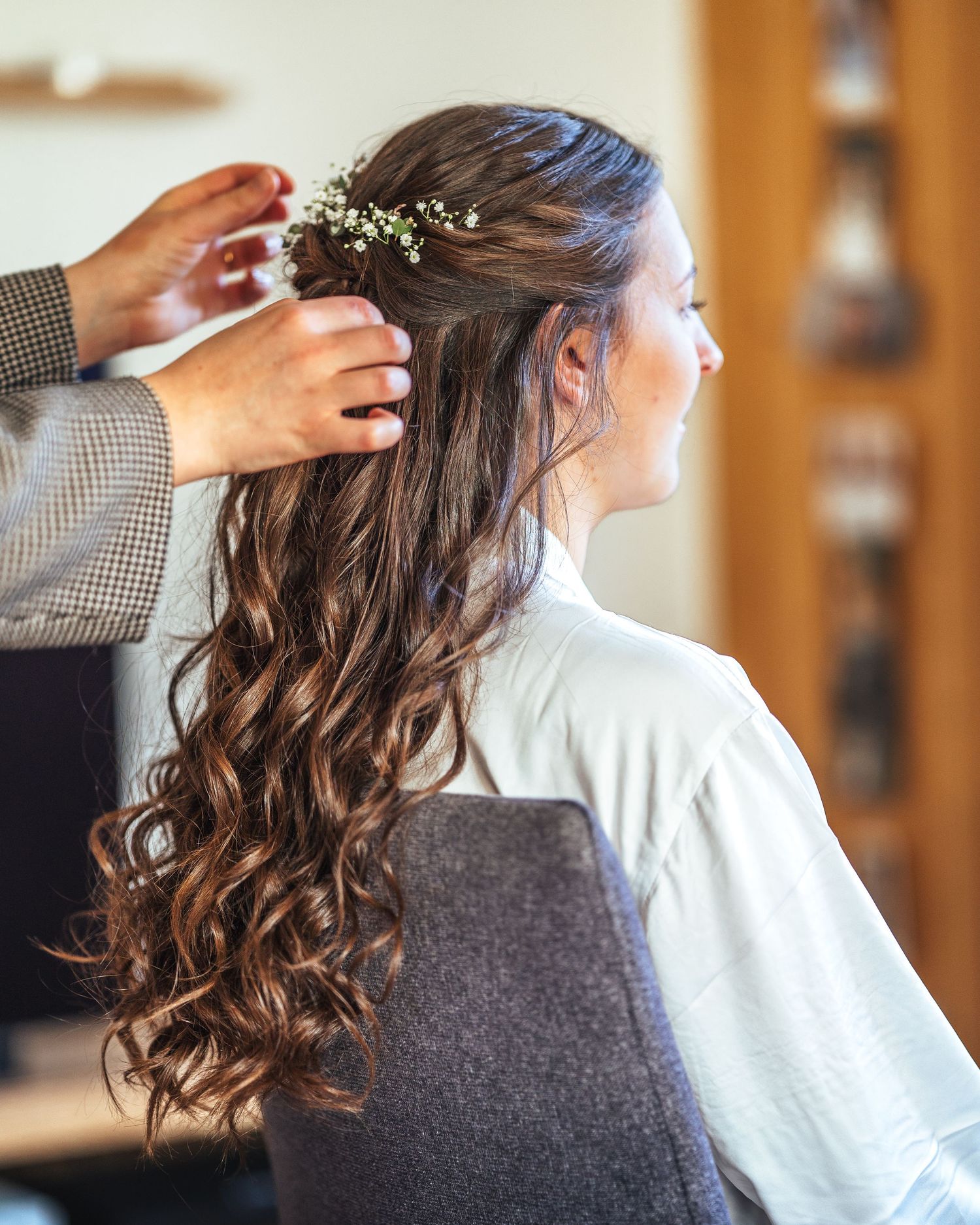 Hairstylist adding delicate white flowers to flowing curled hairstyle for special occasion.