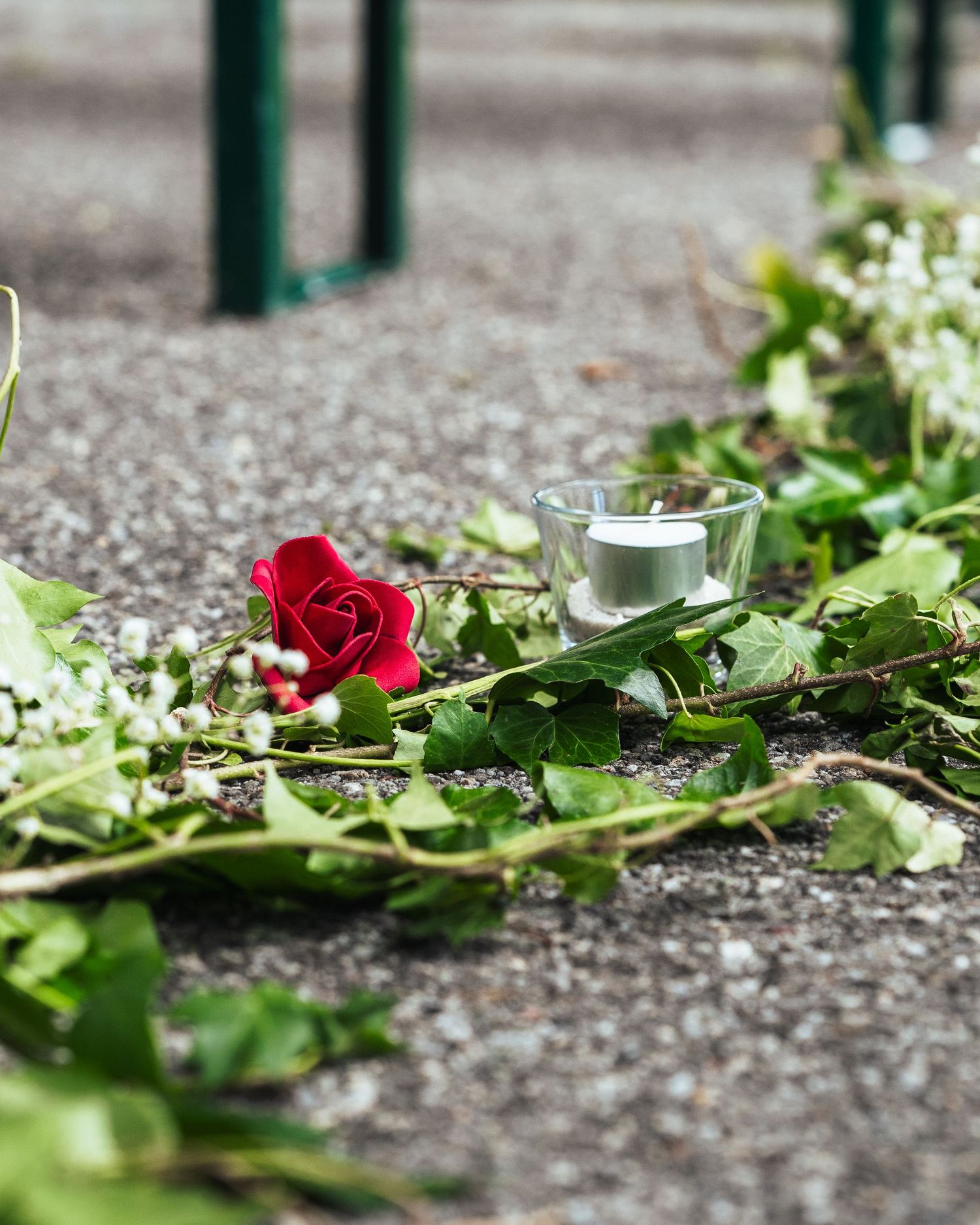 Single red rose and greenery laying on ground with glass tea light holder.