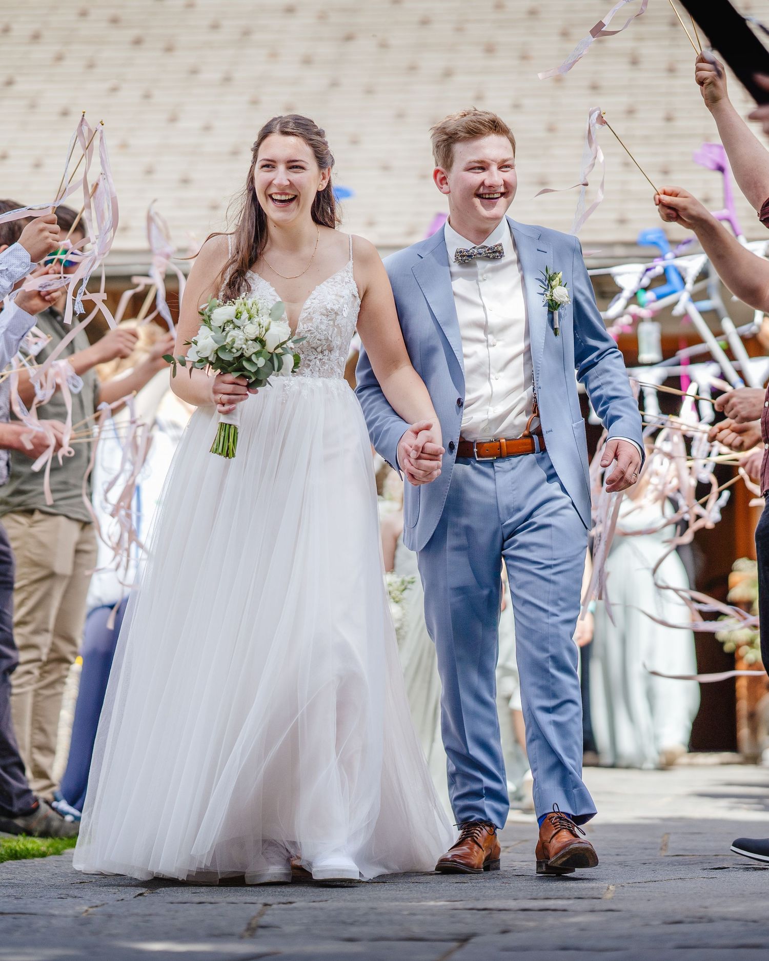 Wedding recessional with couple walking through guest ribbon waving celebration.