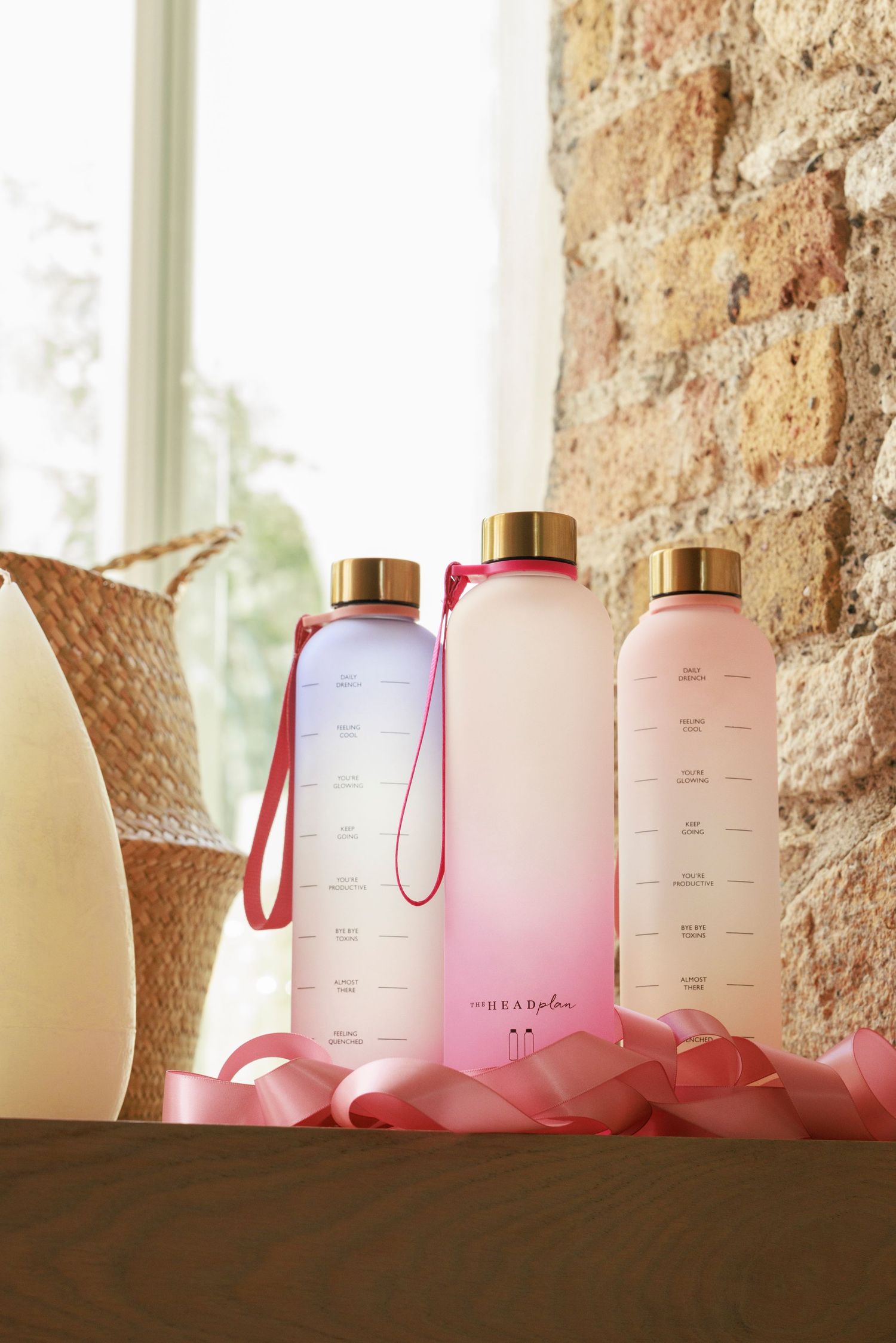 Three glass water bottles with gradient colors and gold lids displayed against a stone wall.