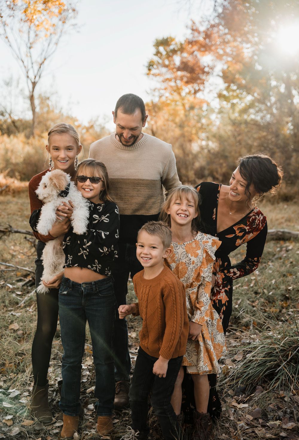 Candid outdoor family portrait with casual poses and natural autumn scenery.