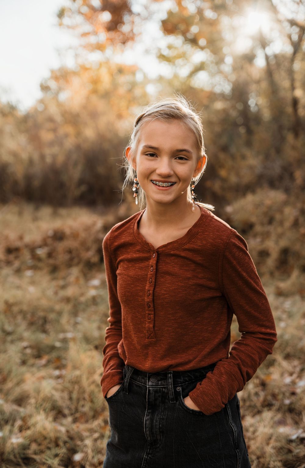Child in rust colored sweater poses casually against autumn background.