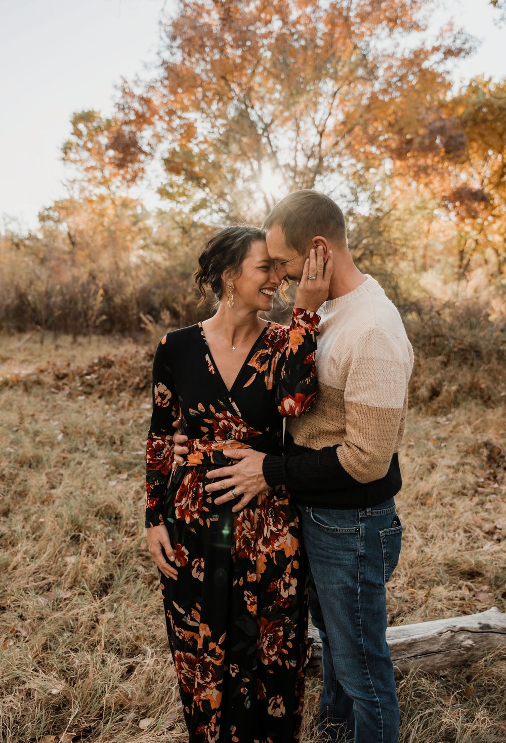 Intimate maternity photo of couple embracing in autumn field at sunset.
