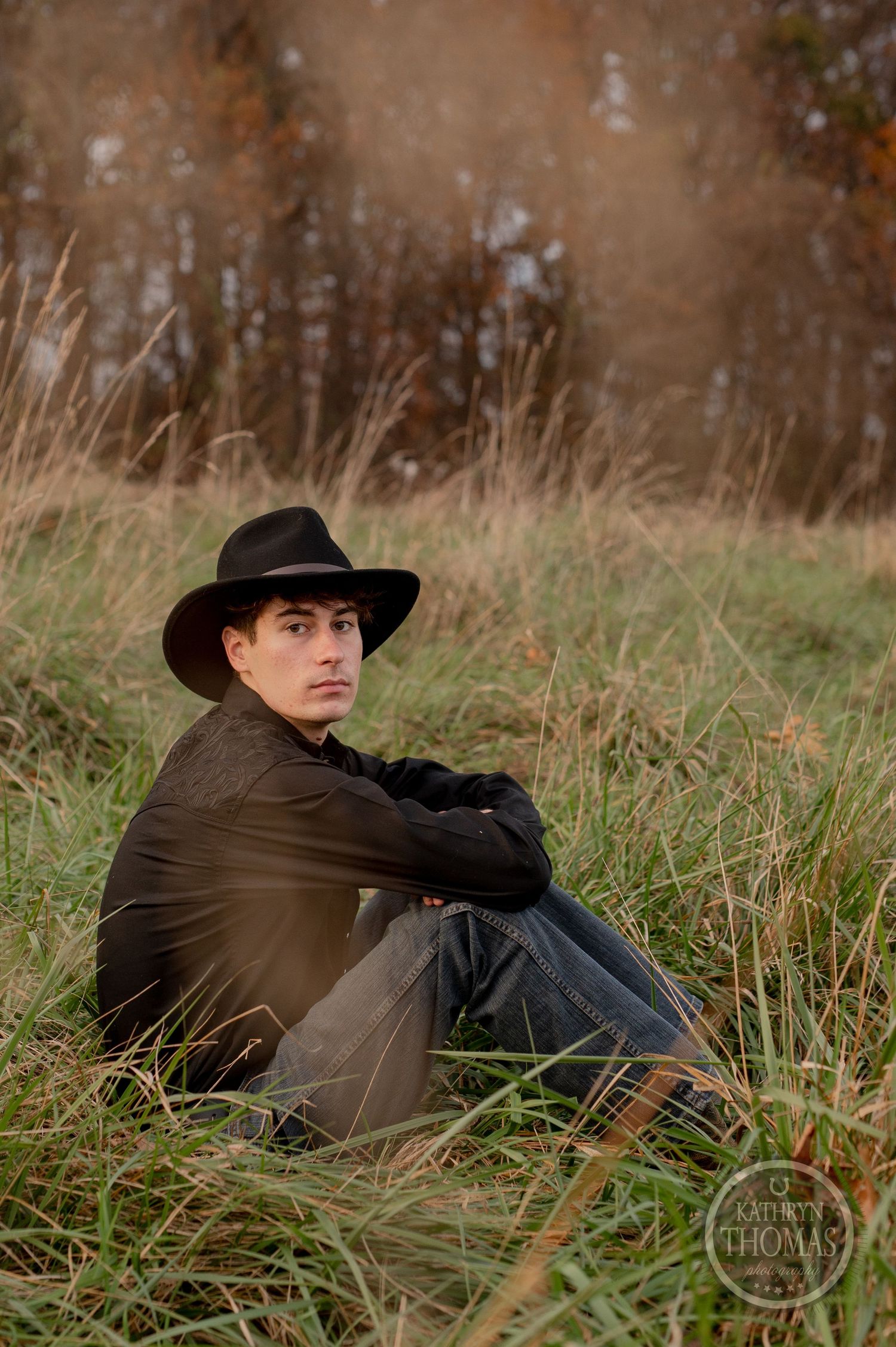 Moody dusk portrait seated in tall grass with warm autumn tones.