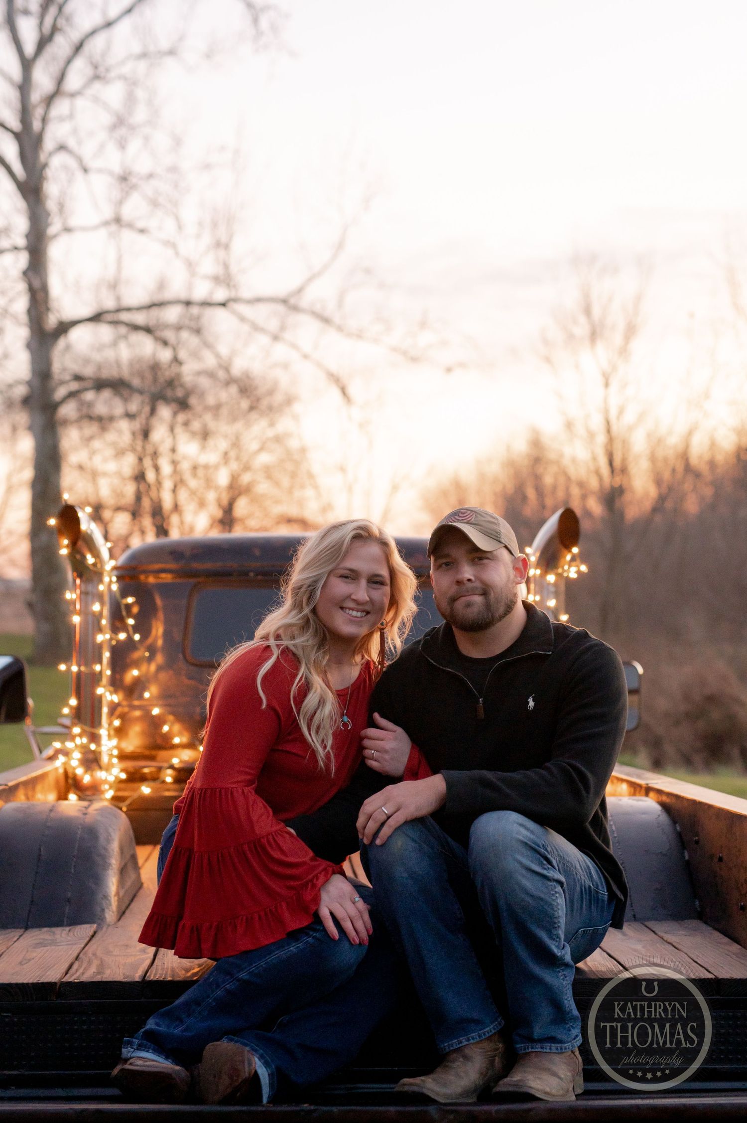 Couple sitting together in back of truck with fairy lights during golden hour.