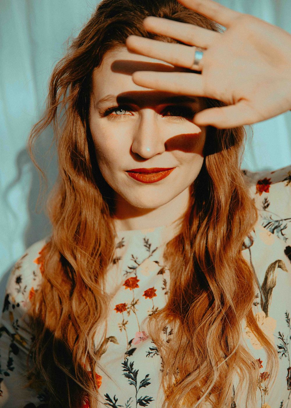 Colorful portrait of woman shielding sunlight from eyes in outdoor photograph.