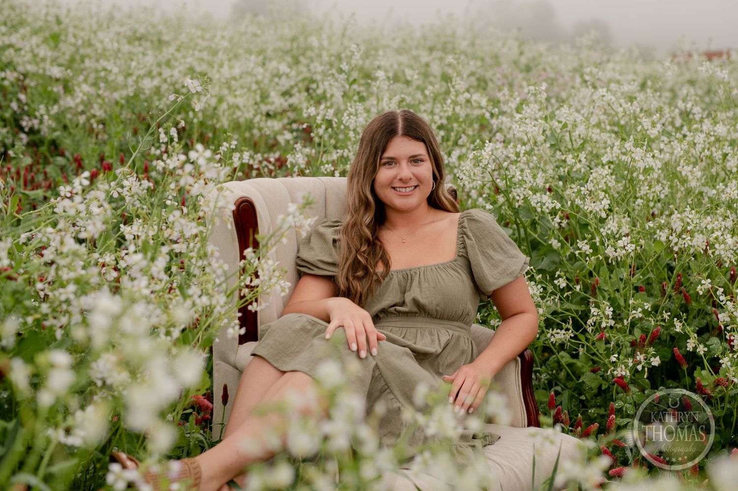 A woman relaxes in an armchair surrounded by blooming wildflowers in a misty field.