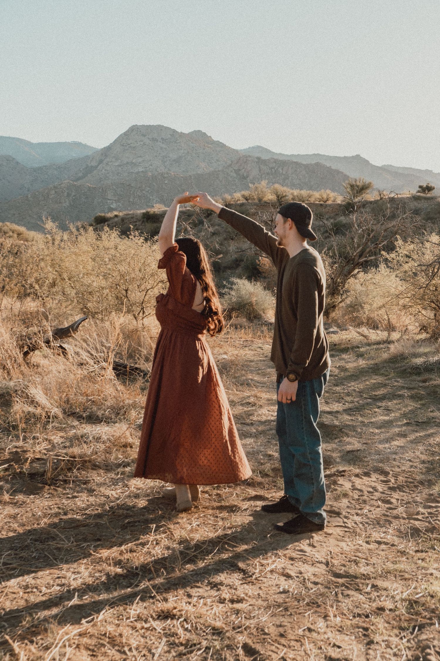 Couple dancing together on a desert trail with mountains in the background.