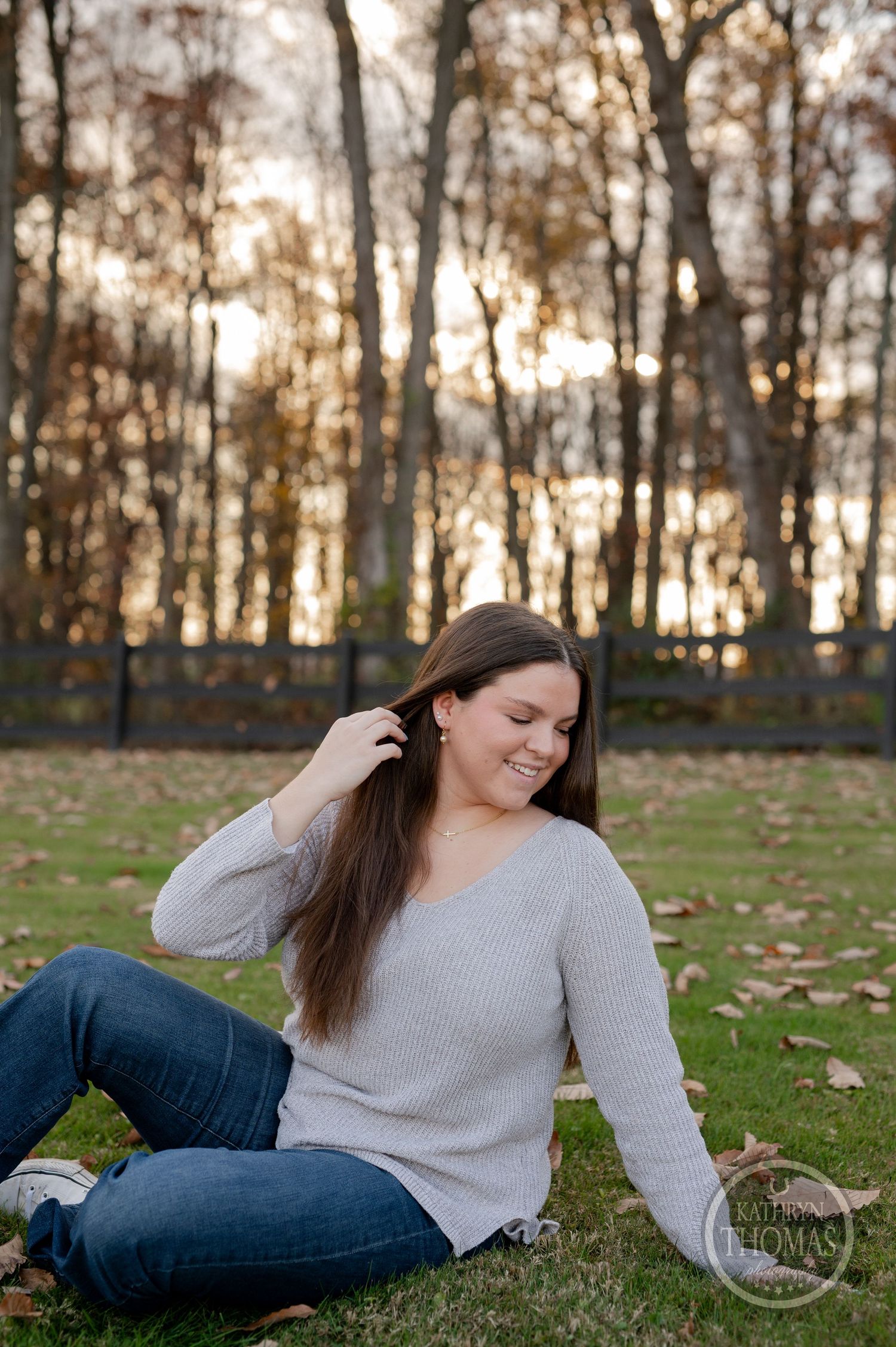 Casual outdoor autumn portrait in gray sweater with sunlit trees and fallen leaves.