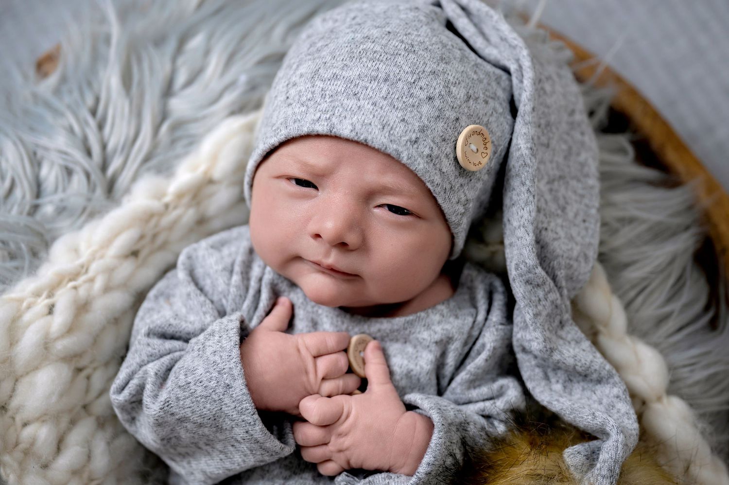Newborn wearing soft gray outfit and beanie while resting on textured fabric.