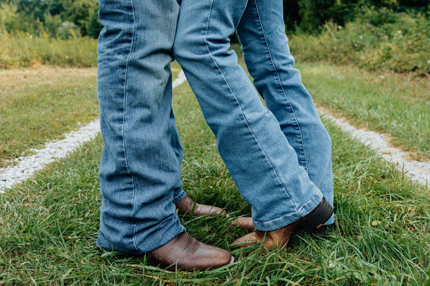 Couple in white outfits holding hands while walking in grassy field at dusk.