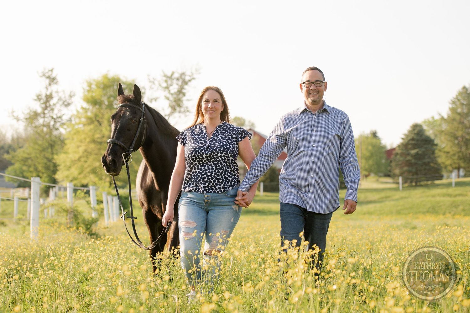 A couple walks through a wildflower meadow with their black horse following behind.