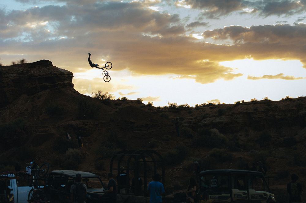 Mountain biker performs jump silhouetted against dramatic sunset sky.