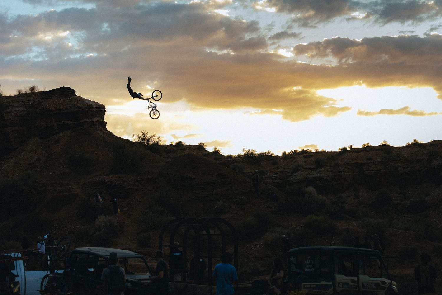 Mountain biker performs jump silhouetted against dramatic sunset sky.