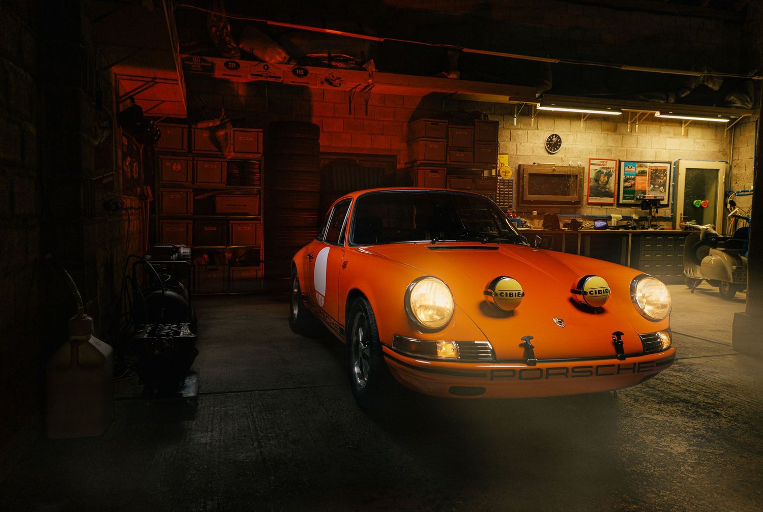 Classic orange Porsche sports car illuminated in dimly lit garage setting.