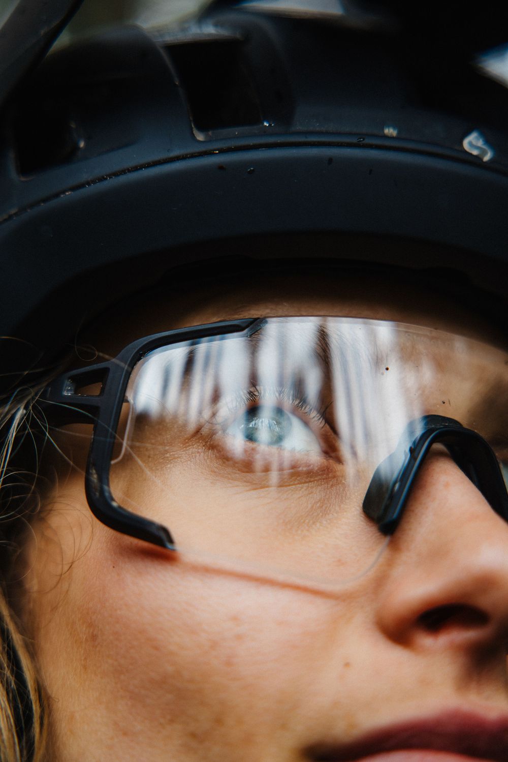 Close-up of cyclist wearing black helmet and clear sports glasses with blue eyes reflected in lens.