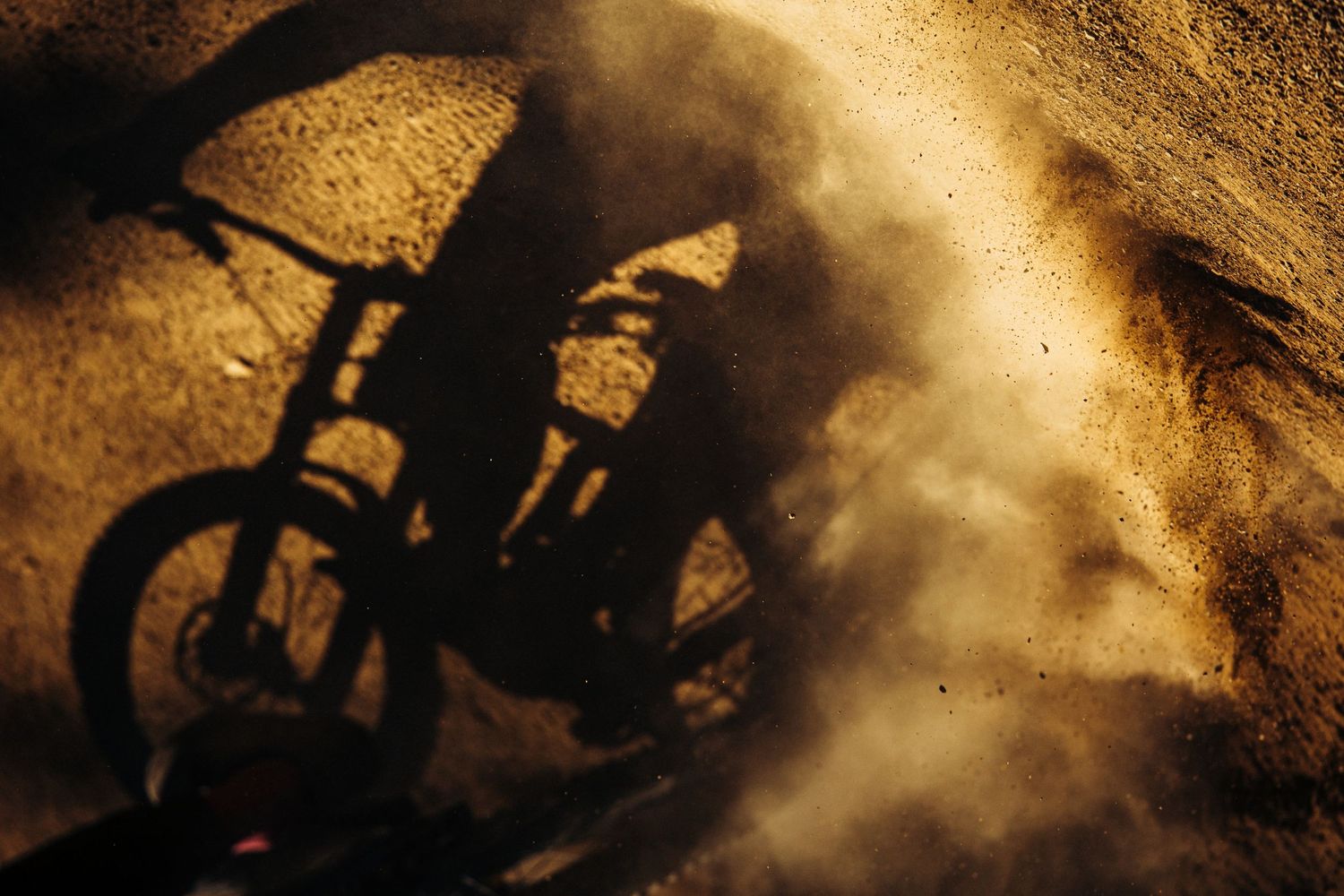 Shadow of a mountain bike casting dramatic silhouette on dusty ground at sunset.