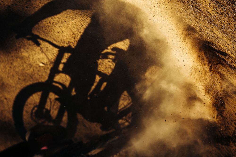 Shadow of a mountain bike casting dramatic silhouette on dusty ground at sunset.