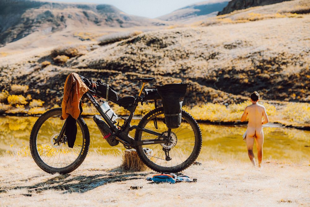 Loaded bikepacking mountain bike parked in scenic desert landscape with rider exploring natural hot spring.