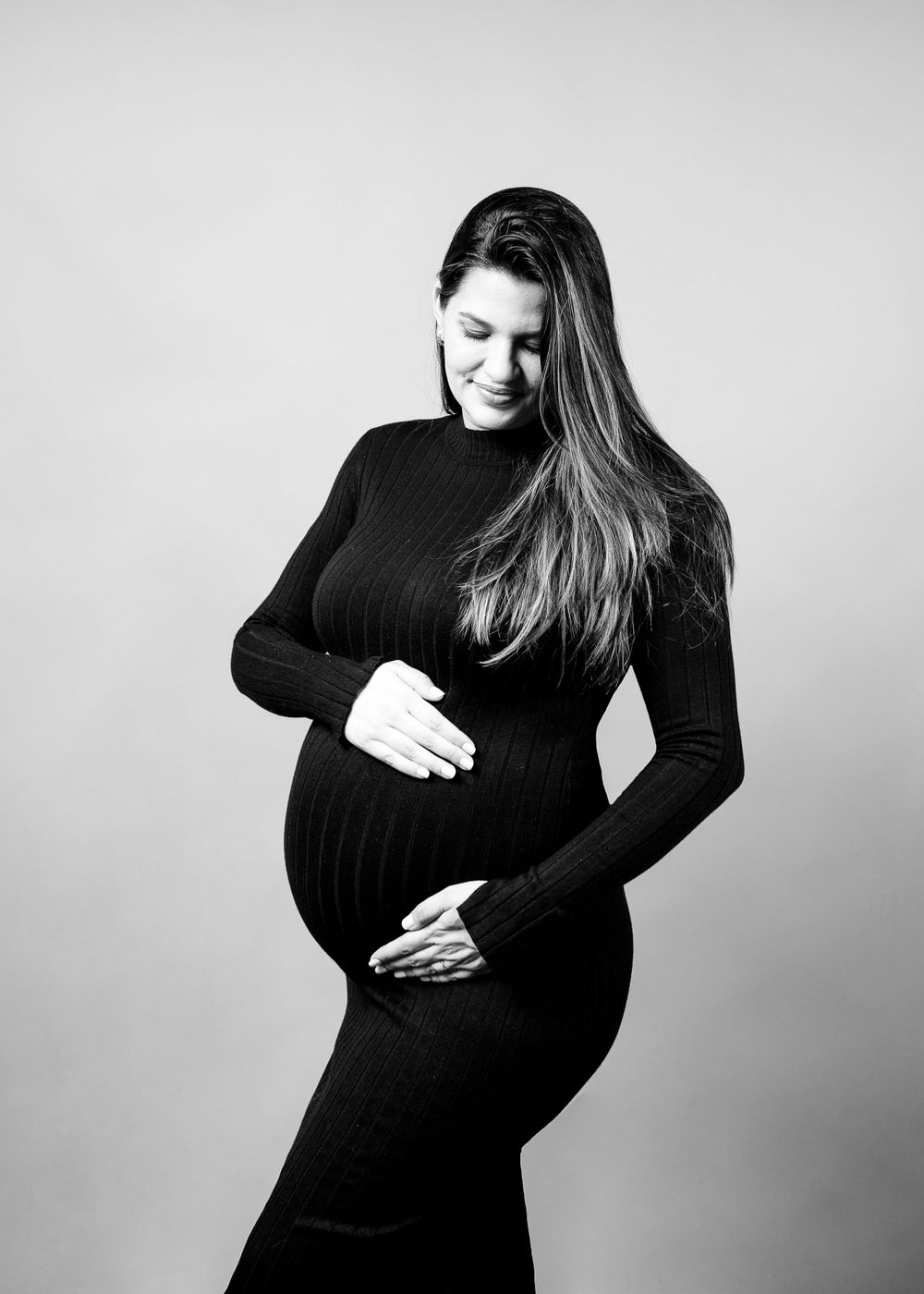 Black and white maternity portrait featuring a woman in a fitted black sweater dress.