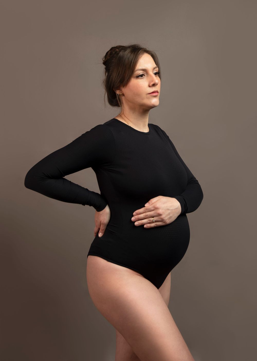 Maternity portrait of person in black bodysuit against neutral background.