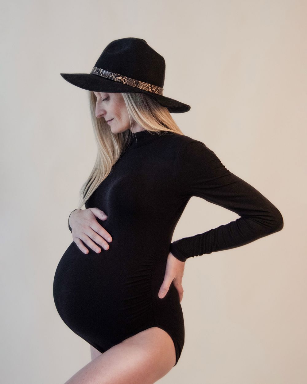 Maternity fashion photo with a black fedora hat and fitted bodysuit.