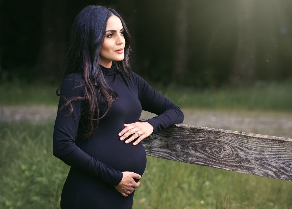 Outdoor maternity portrait in black sweater against rustic wooden fence.