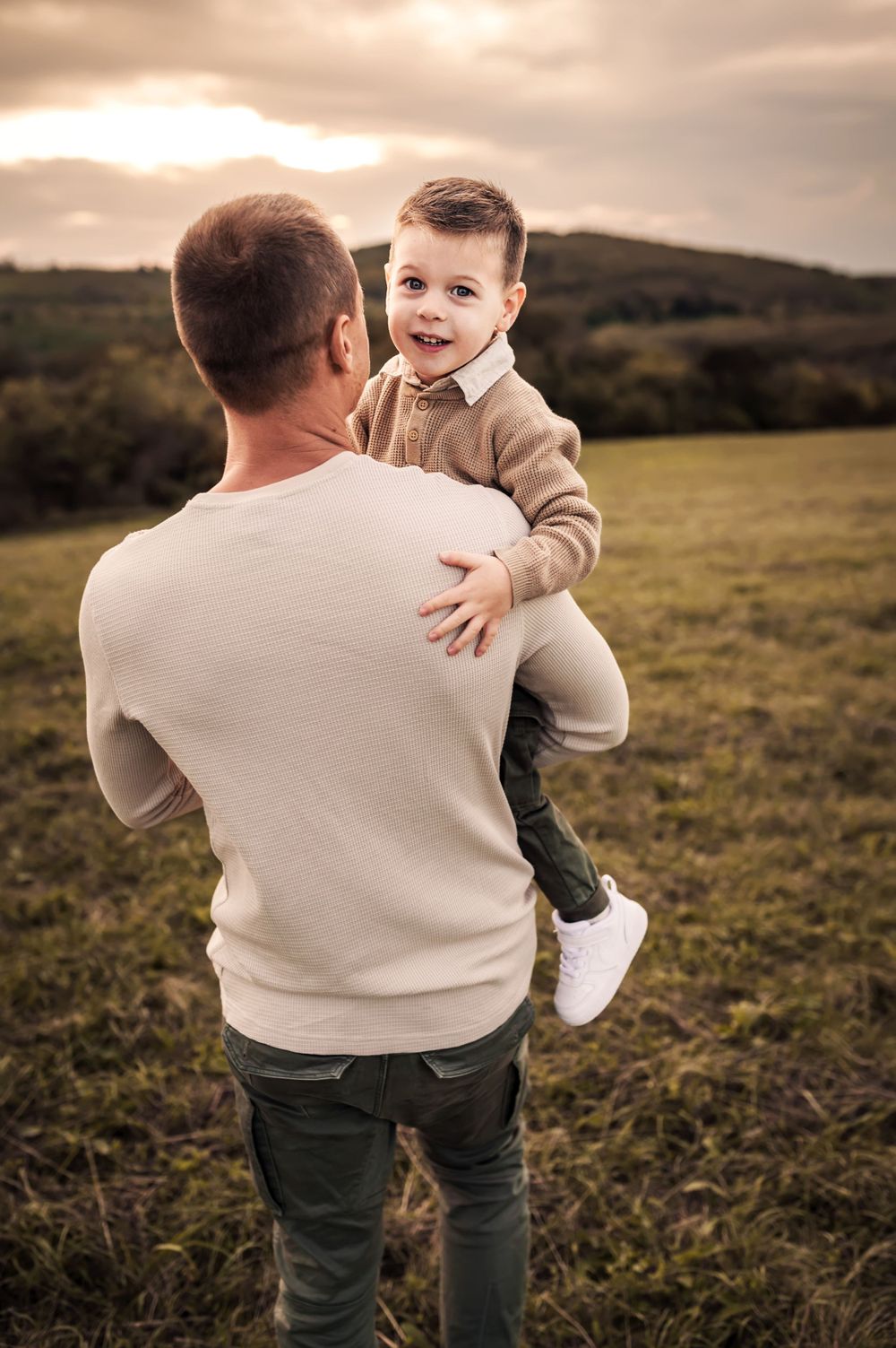 A tender moment captured between parent and child in a sweeping countryside field during golden hour.