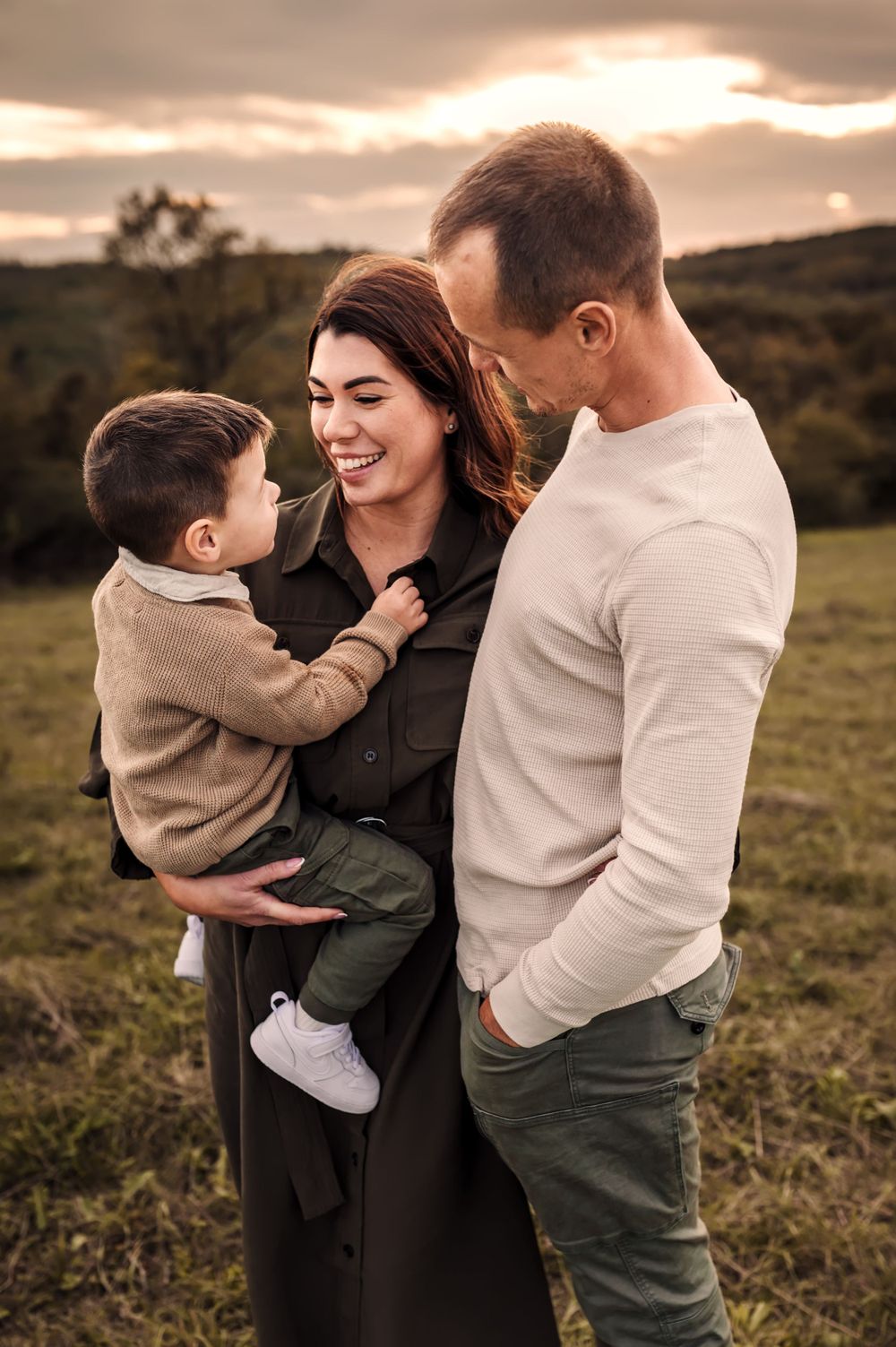 Family shares joyful moment together outdoors during golden hour sunset in grassy field.