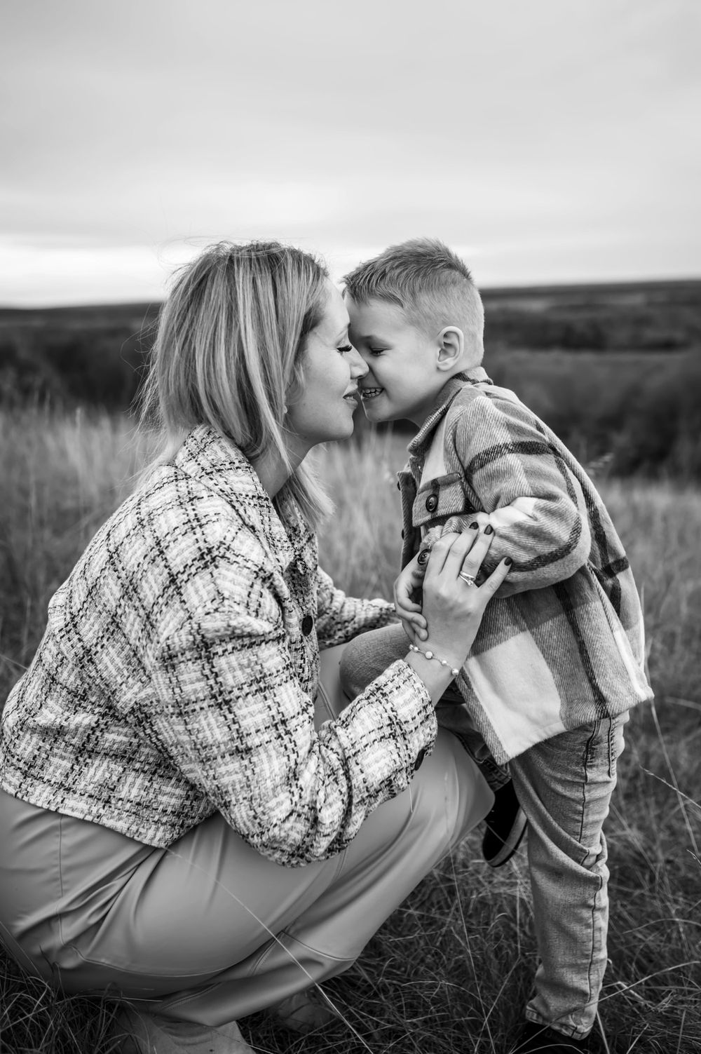 A tender black and white portrait of parent and child sharing an intimate moment together in a grassy field.