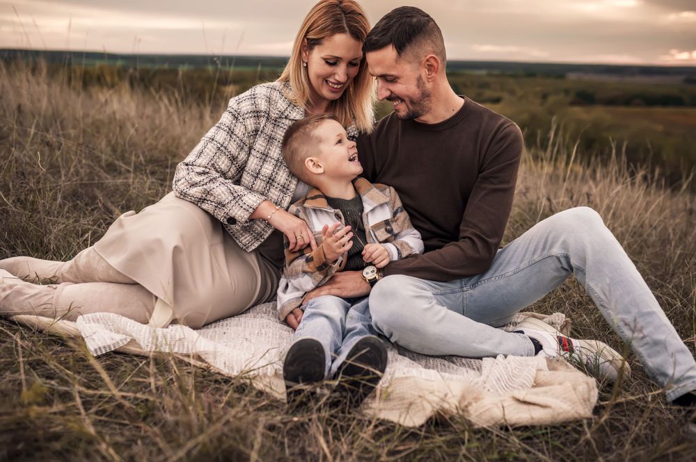 Family sits together on blanket in golden field during sunset photo session.