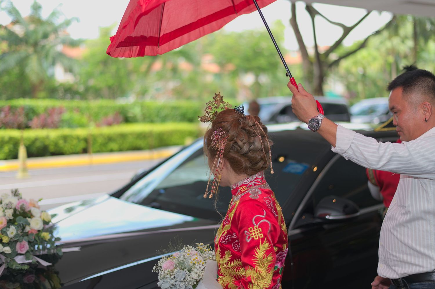 A wedding moment captured outdoors with a red umbrella and formal attire.