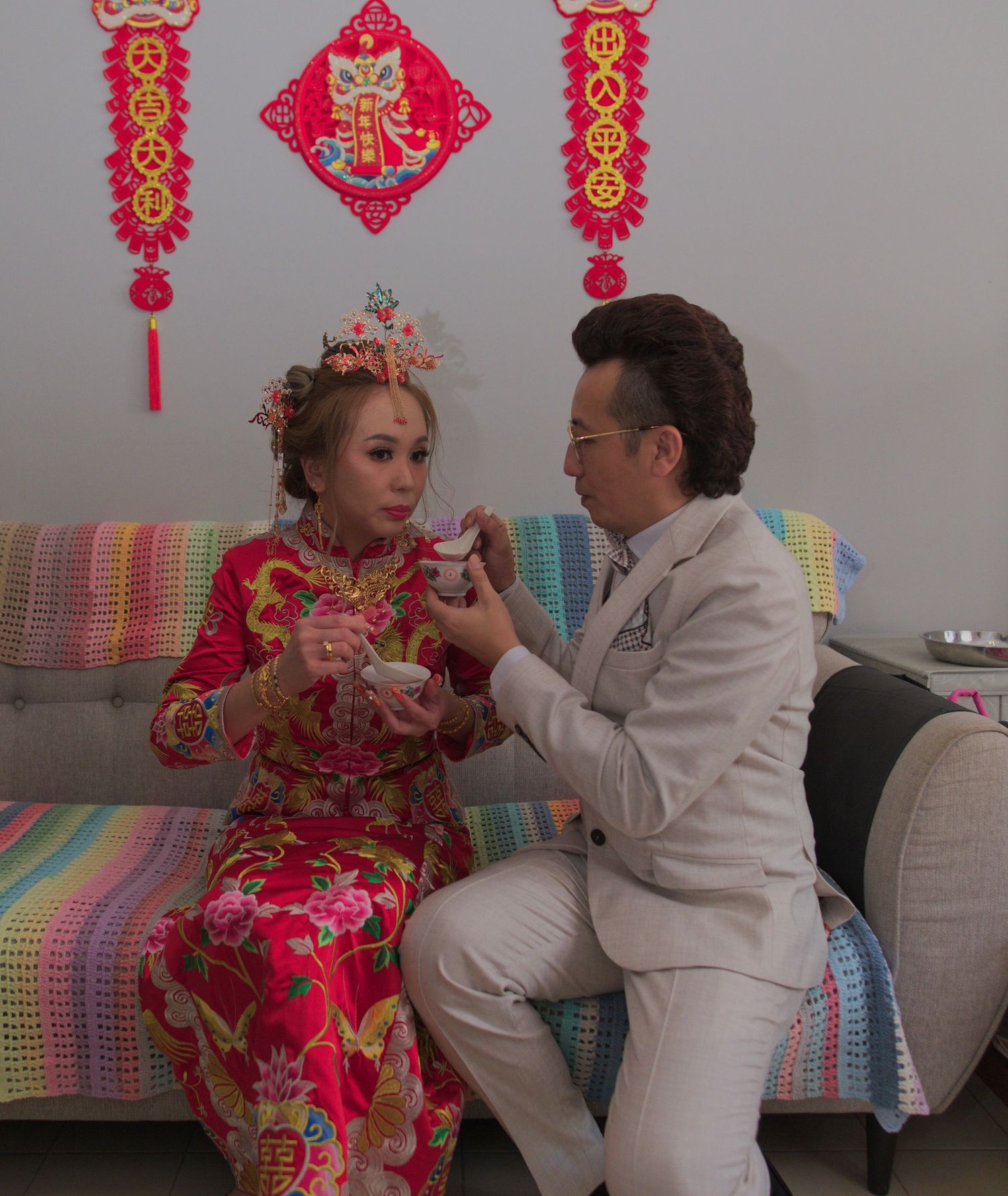 Couple in traditional wedding attire sharing a moment on a colorful couch with Chinese decorations.
