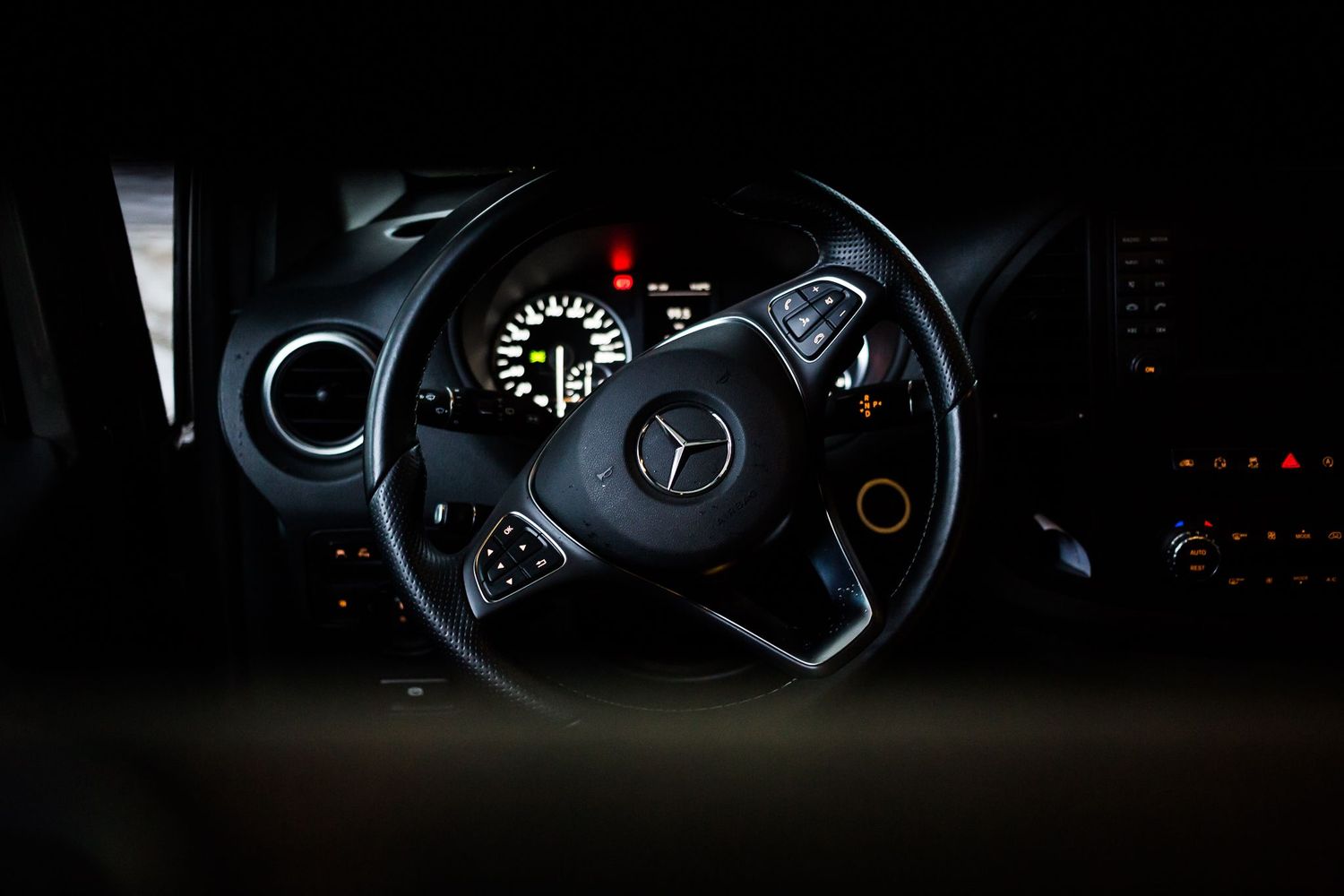 Dark interior shot of a Mercedes-Benz steering wheel and dashboard instruments.