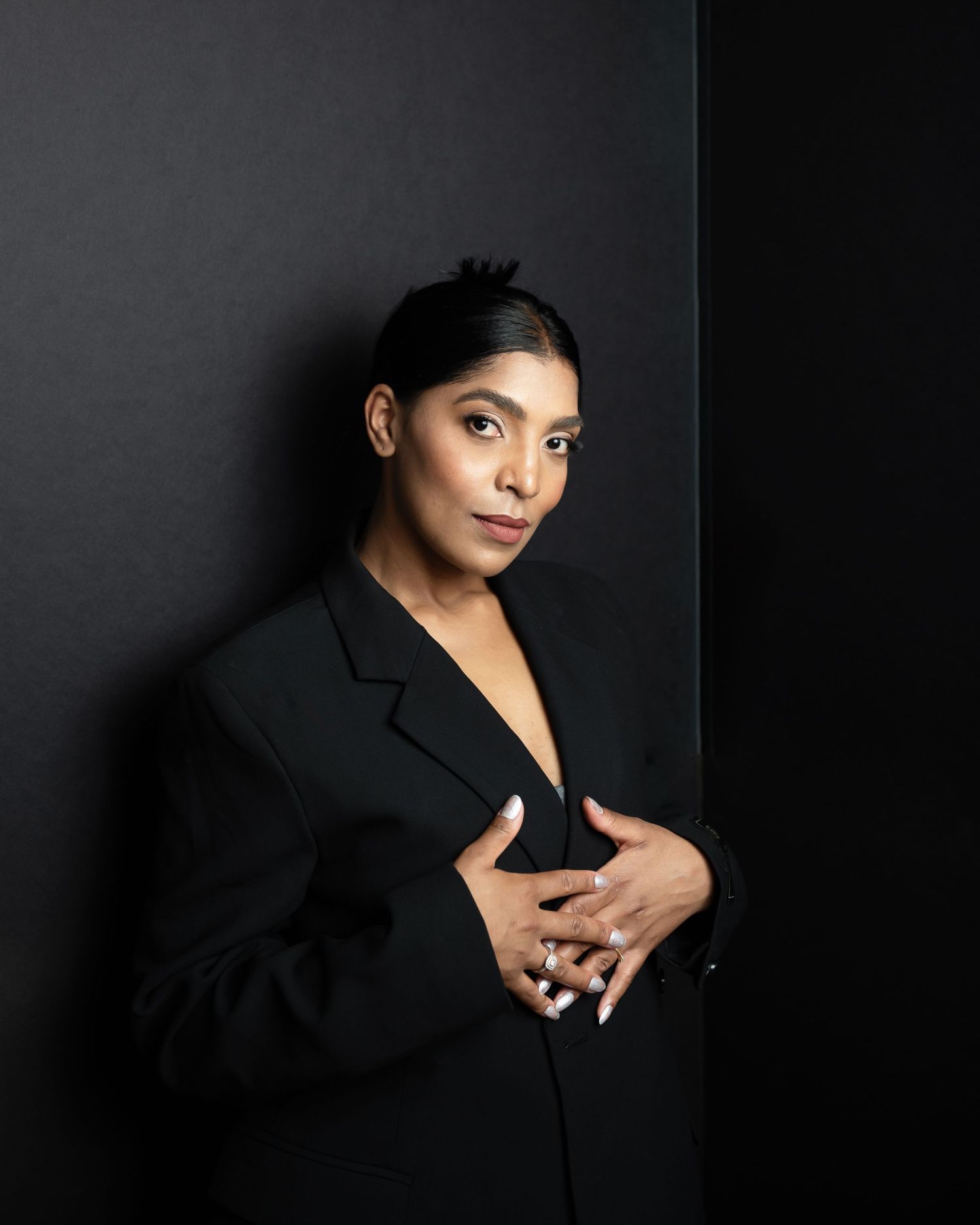 Professional headshot of woman in black blazer against dark dramatic background.