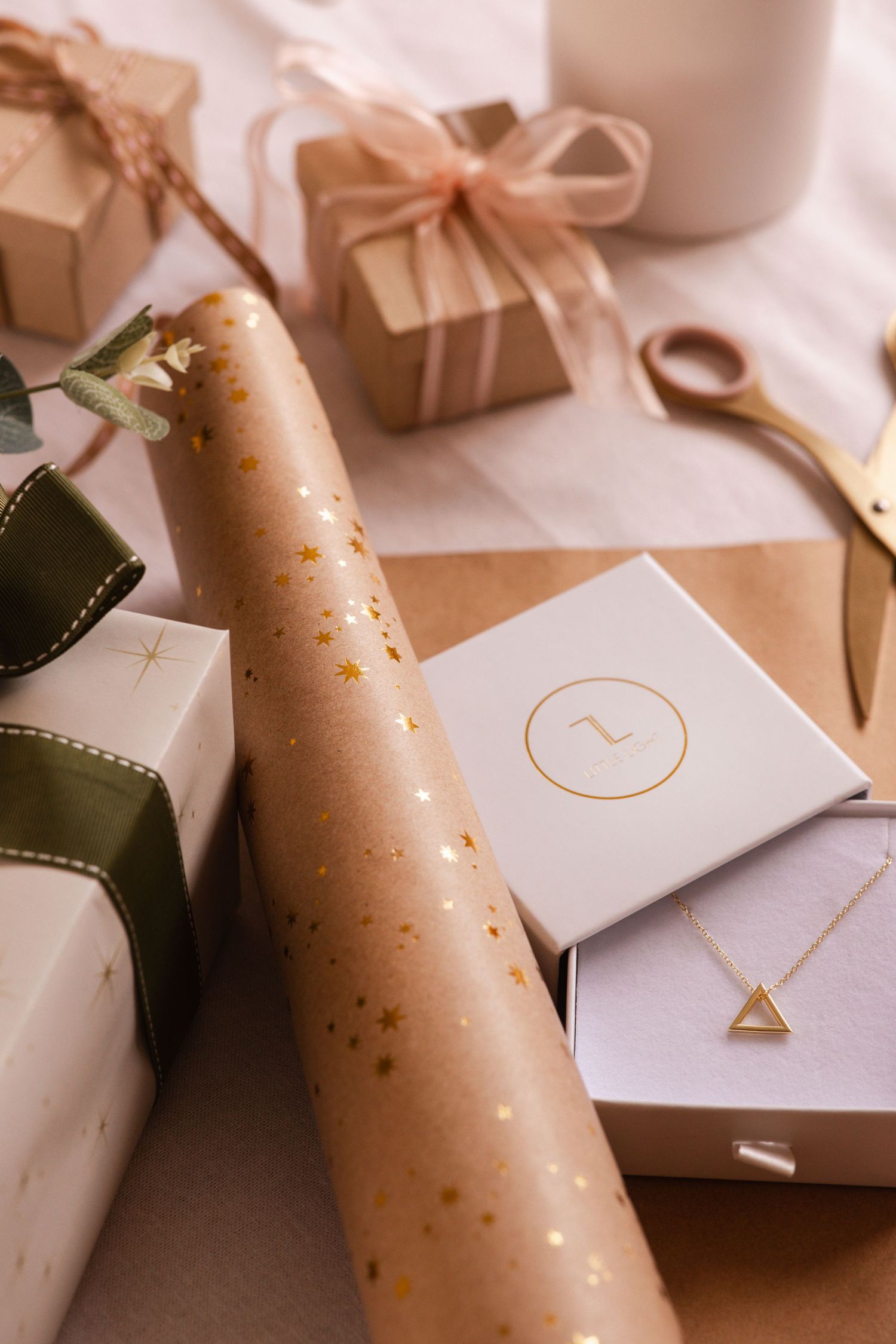 Wrapped presents with gold-speckled paper and jewelry box displaying minimalist triangle necklace. Element of Christmas gifting.