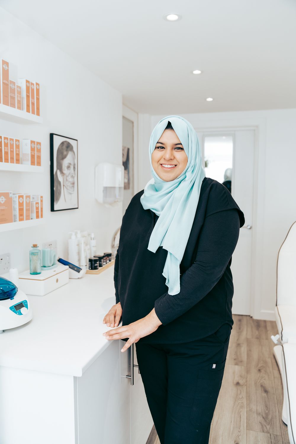 Aesthetics nurse standing in clinic, leaning on the counter, smiling for portrait.