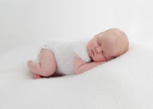 Peaceful newborn baby sleeping on a soft white fluffy blanket, wrapped in a cozy white wrap.