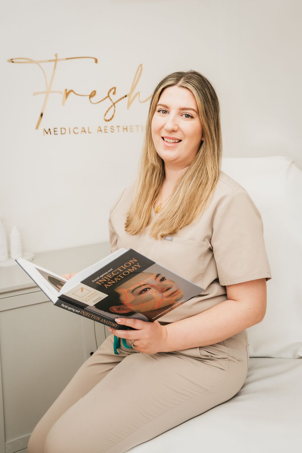 Aesthetic nurse sitting on medical chair holding medical literature smiling for portrait.
