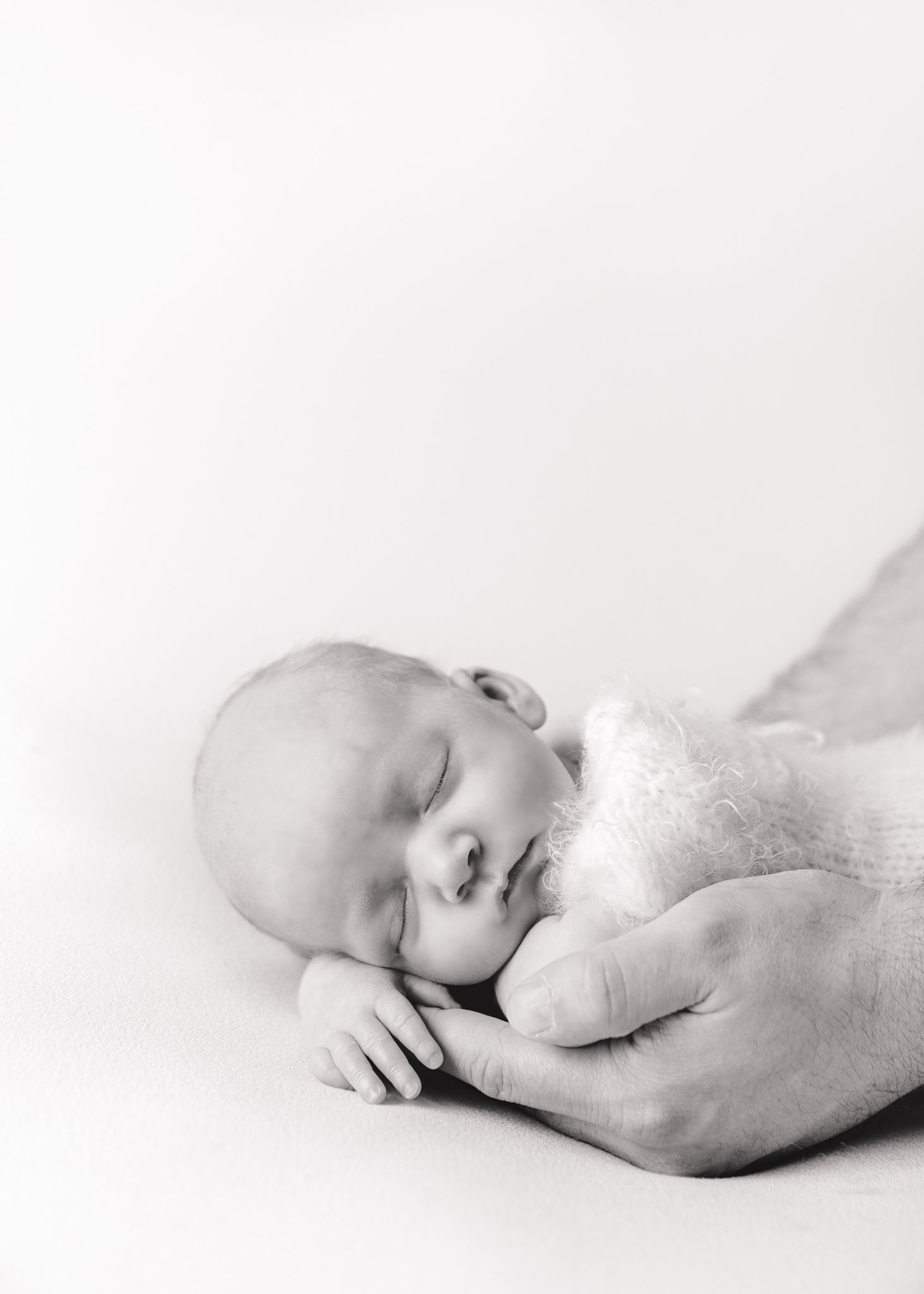 Newborn baby sleeping. Dads hand holding him.