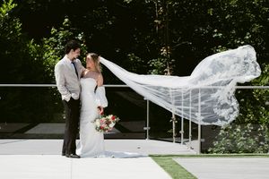 Bride and groom share a romantic moment outdoors as her long veil flows in the wind at their elegant wedding venue.