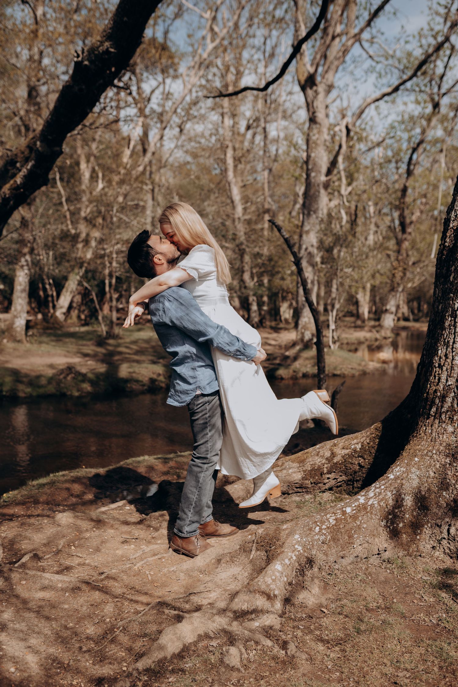 Couple embracing near a tree by a stream in a natural outdoor setting.