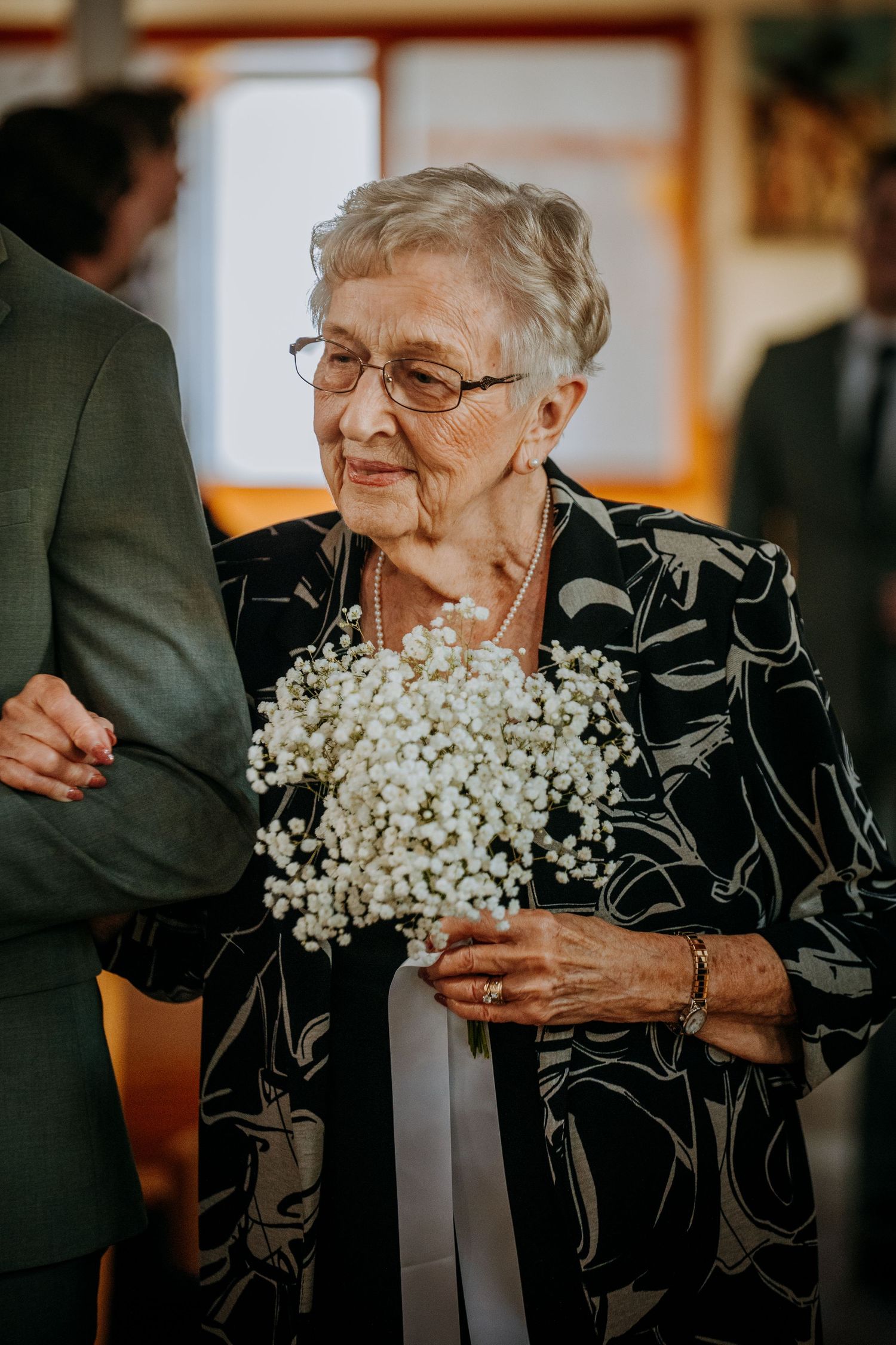 Elegant guest in black floral dress holding delicate baby's breath bouquet at formal event.
