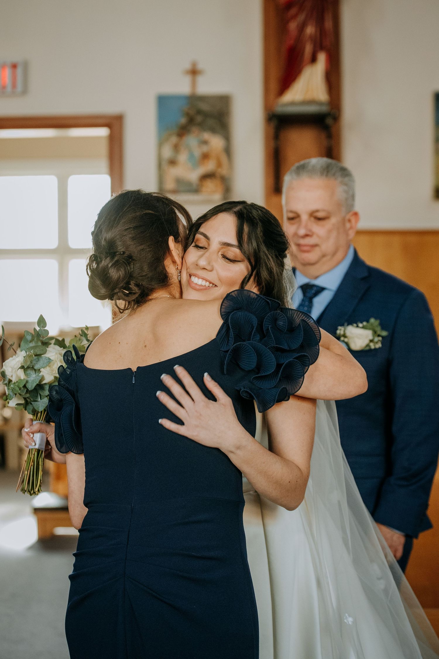 Two women embracing during emotional wedding ceremony moment in church setting.