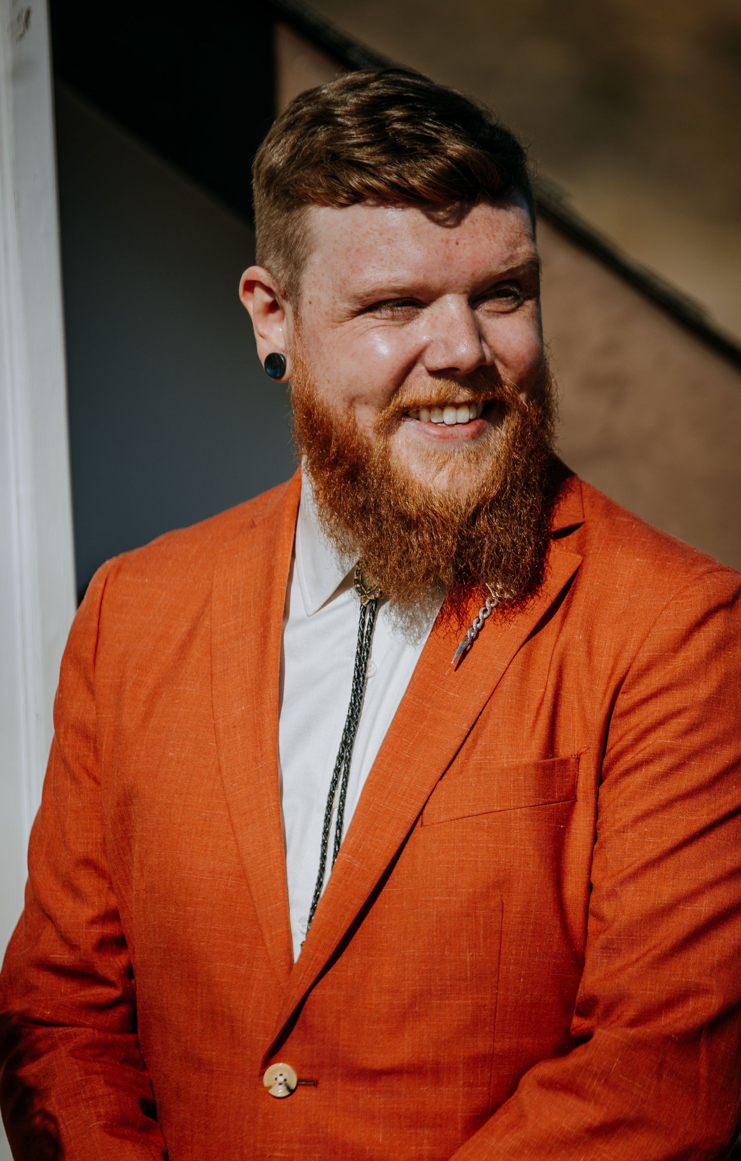 A person in a vibrant orange suit jacket smiles warmly at the camera.