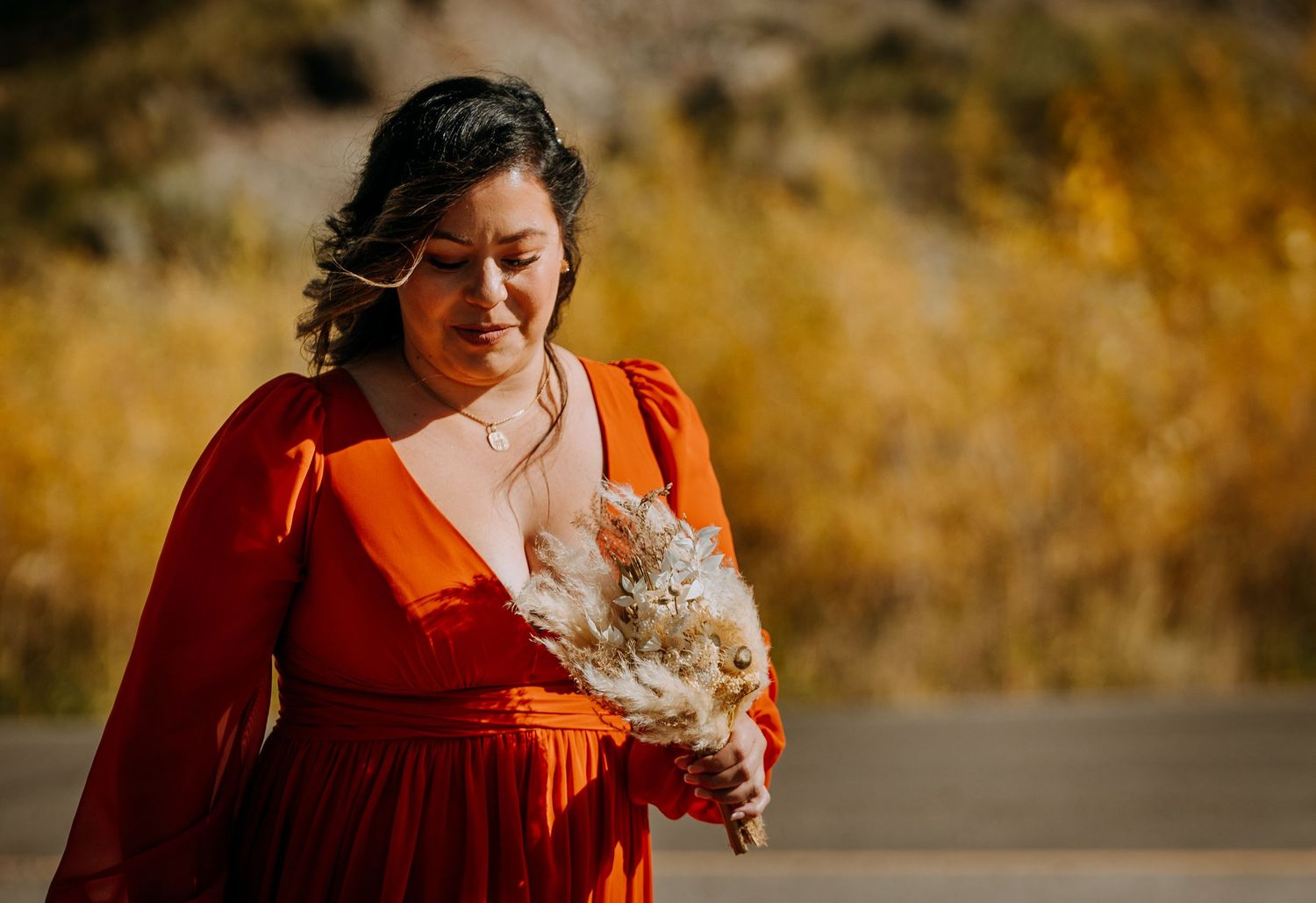 A person in a red dress holds a dried flower bouquet in outdoor sunlight.