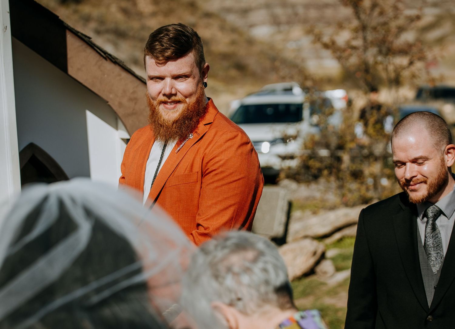 Two people in formal attire stand together during an outdoor ceremony.