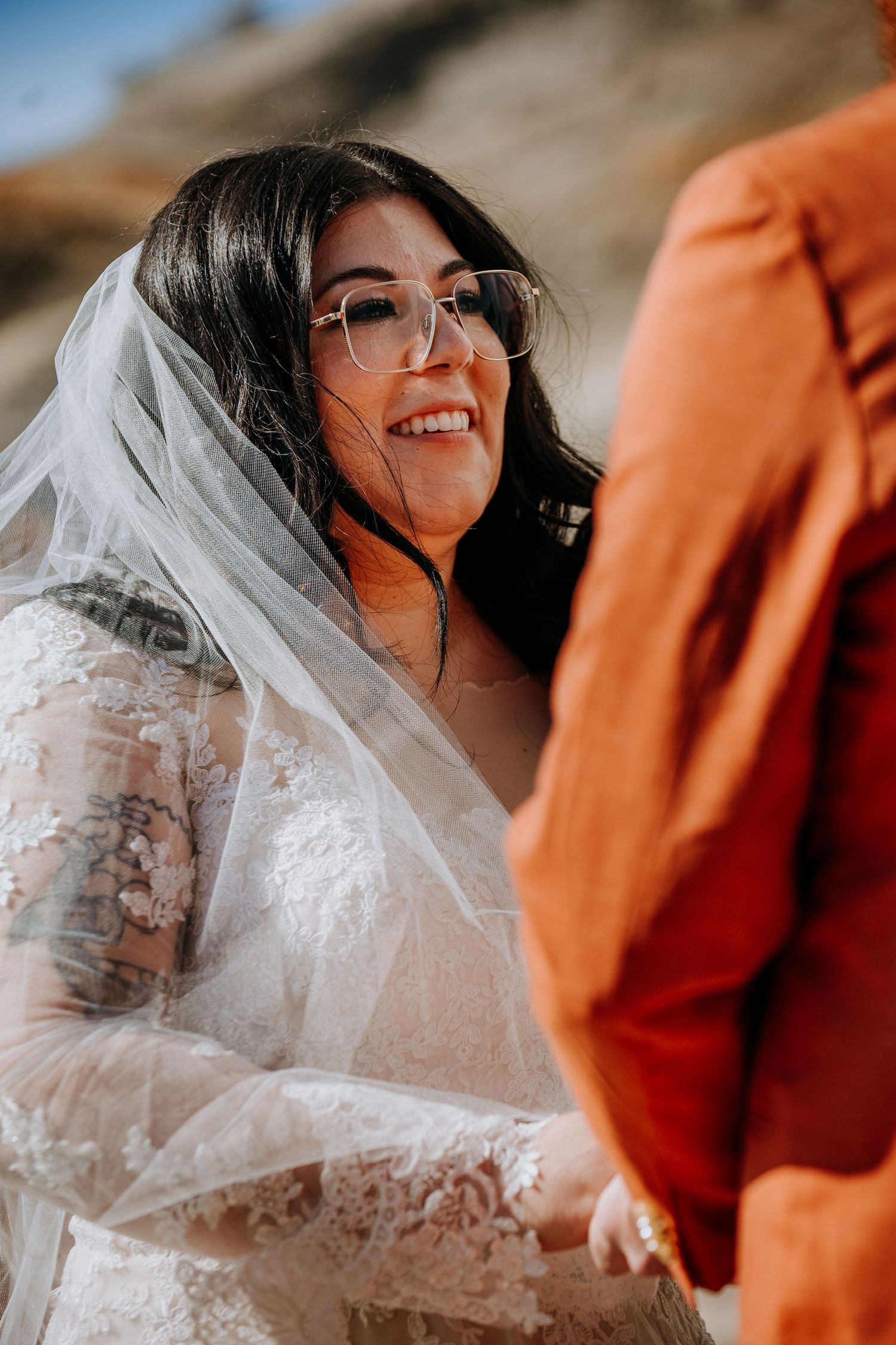 A bride in a lace dress and veil smiles during her wedding ceremony.